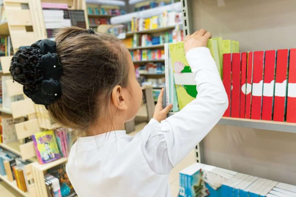 A child browsing books on library shelves.