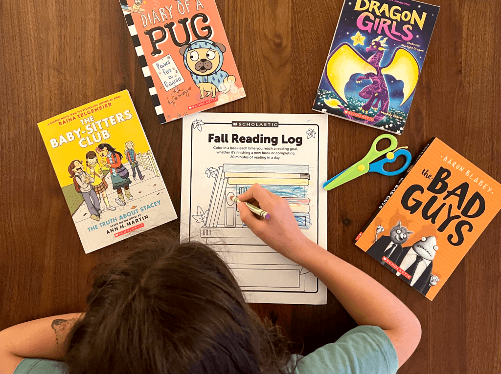 A student completing a fall reading log surrounded by books.